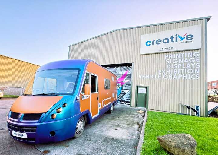 The transformed campervan with its bold copper orange and pearlescent lavender wrap parked outside our Creative Solutions workshop