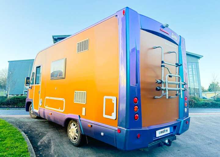 The transformed campervan with its bold copper orange and pearlescent lavender wrap parked outside our Creative Solutions workshop